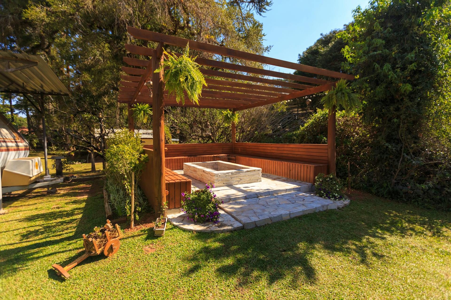 A wooden garden gazebo with a stone firepit in the middle.