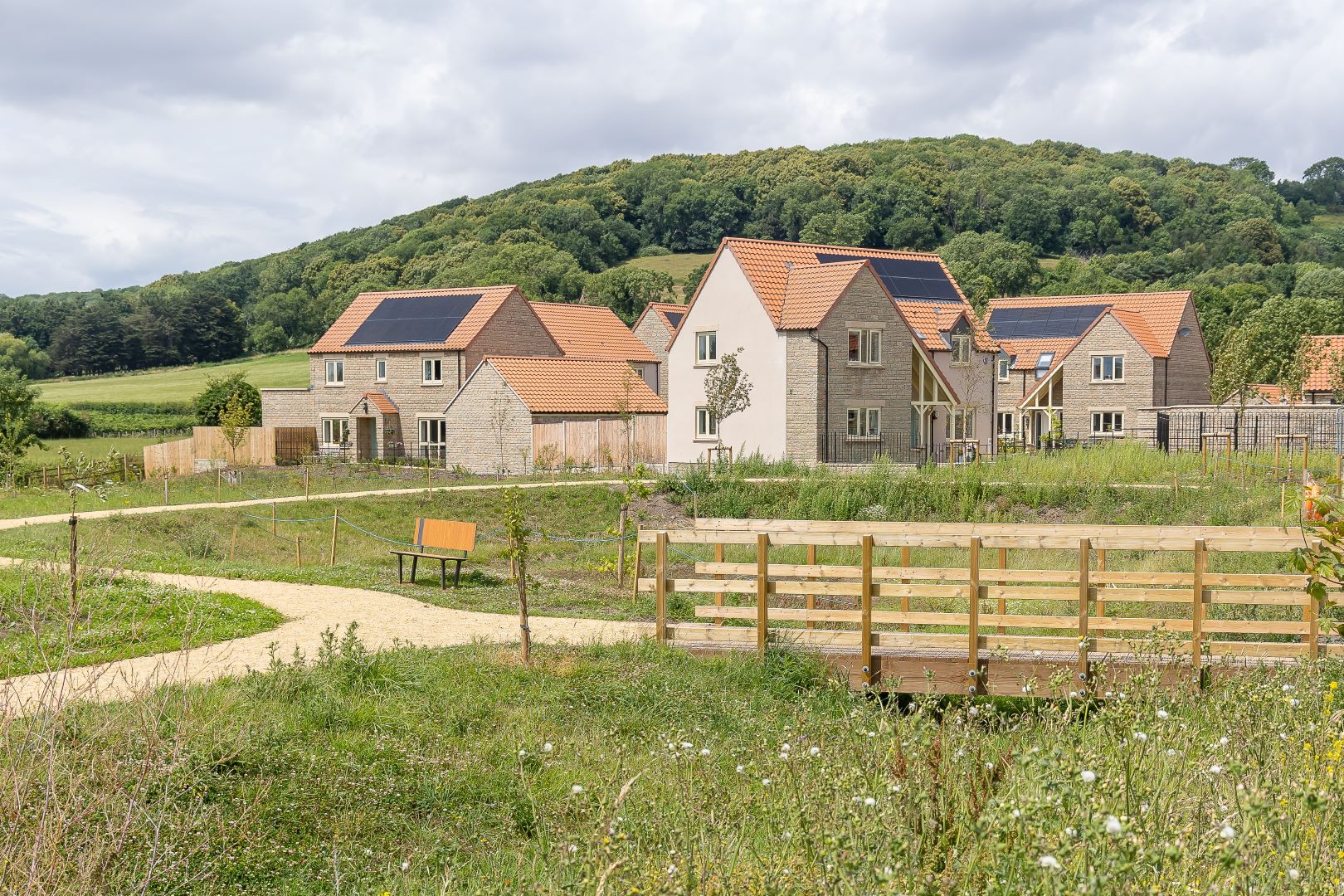 Houses with red roofs sitting in a meadow with wood fencing and pathways