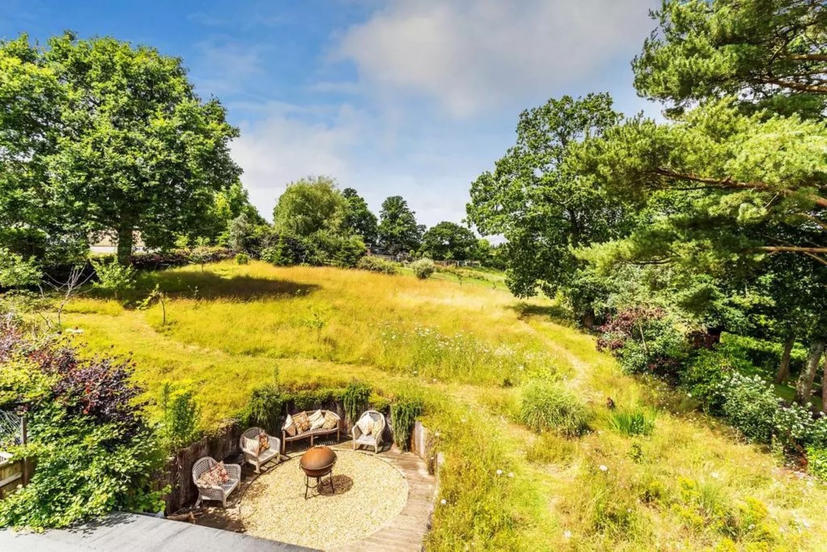 Sunken seating area in a grassy meadow and trees on the boundaries.