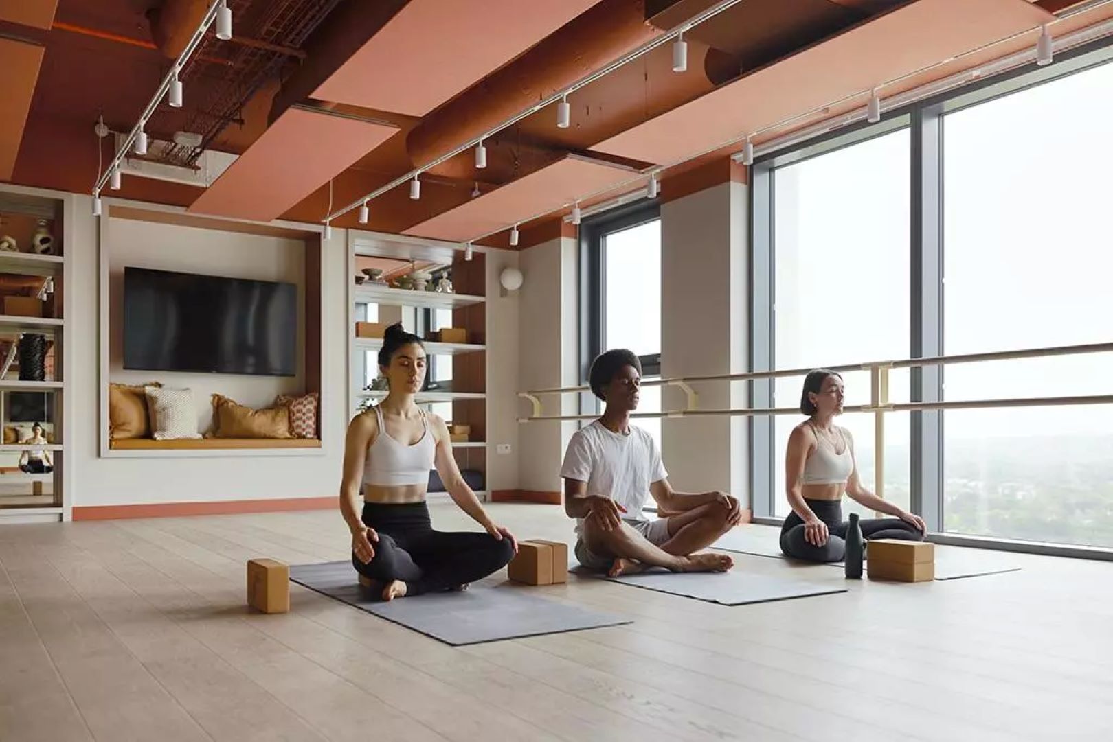 Three people in a yoga studio sitting in hero pose.
