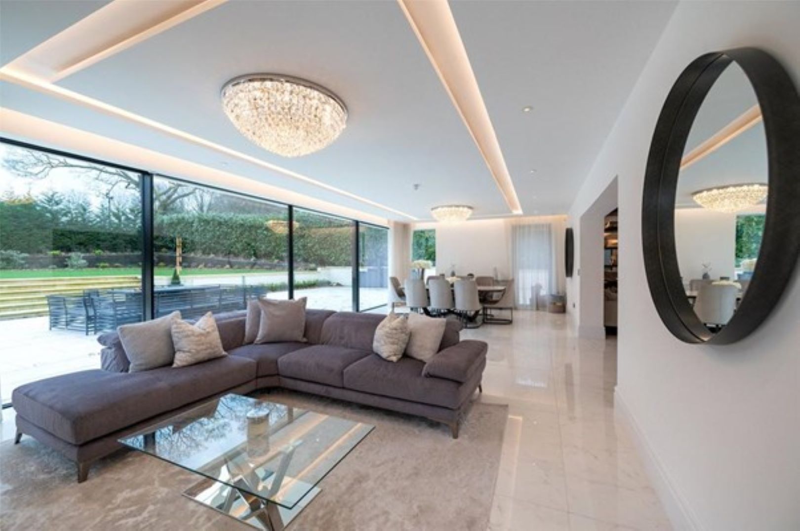 A long sitting room with grey L shaped sofa and strip lighting over head