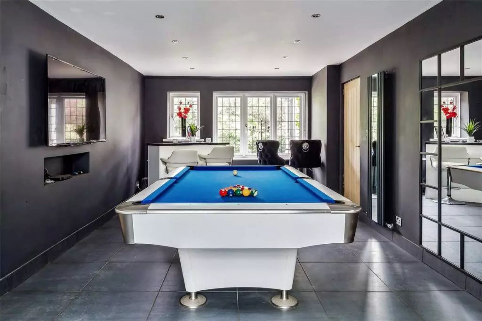 Games room with blue pool table, dark walls and a white bar in the back left corner