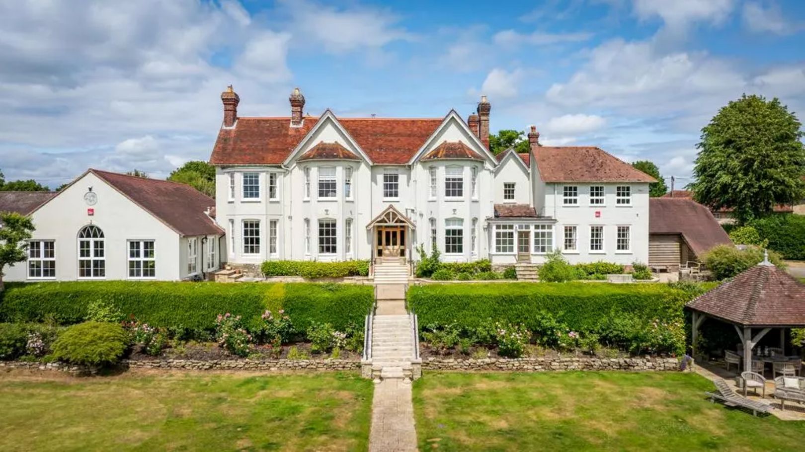 Large white house with hedges and a gravel path leading to it. 