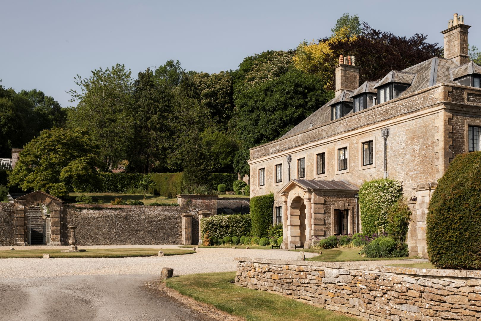 An old, stone house with carriage driveway and trees to the back. 
