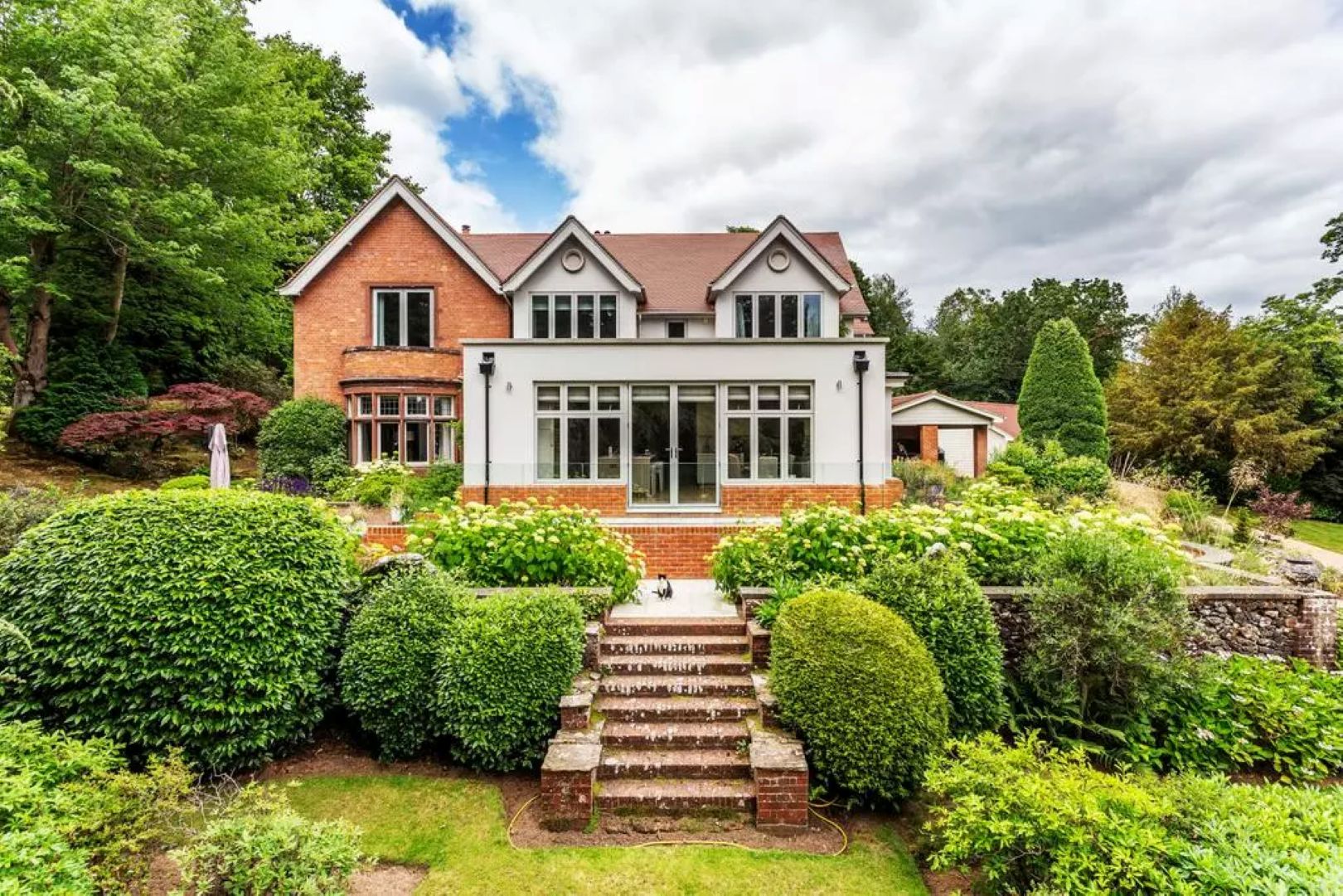 While and brick house surrounded by trees and shrubs