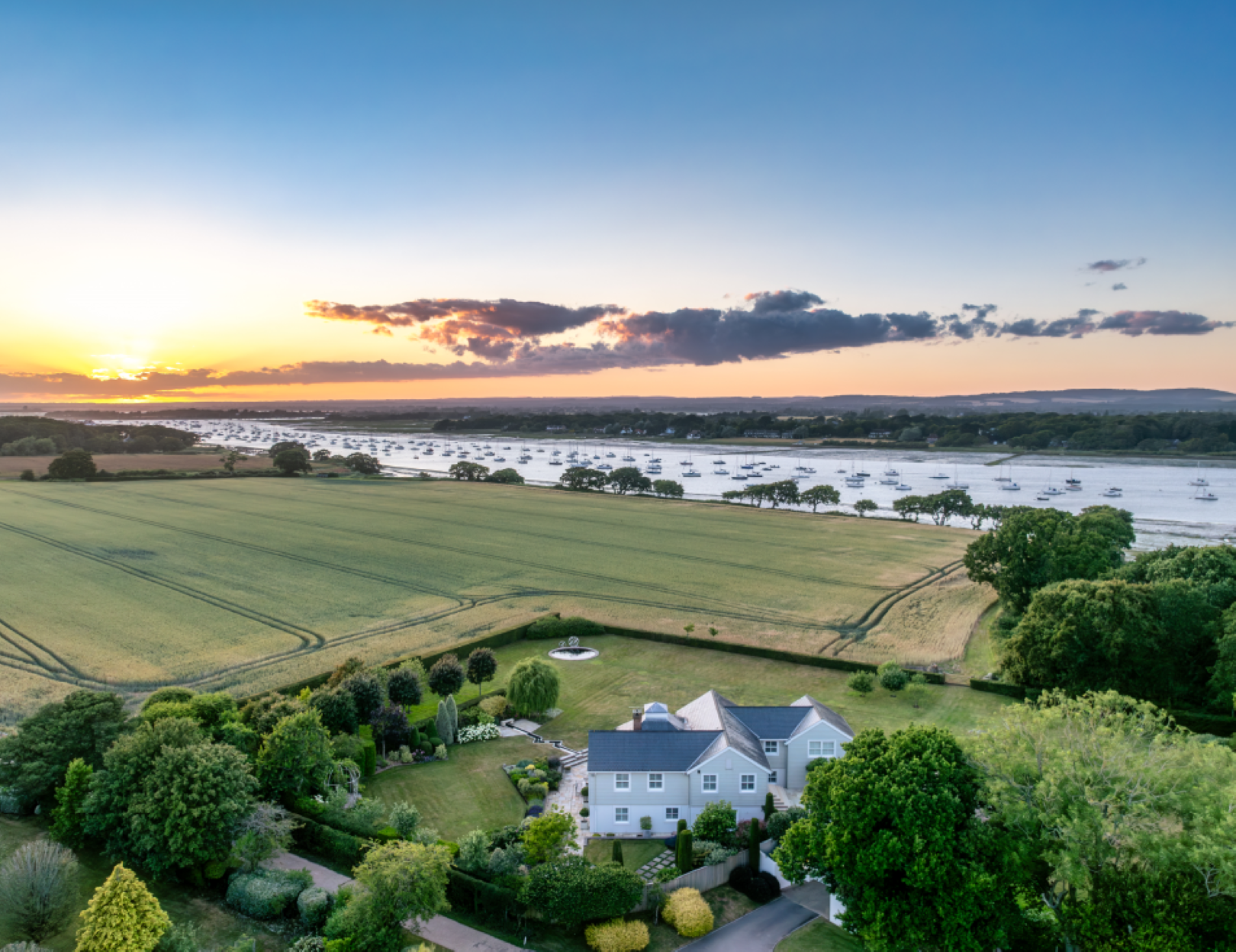 A white house with views overlooking green fields and Chichester Harbour in the background.