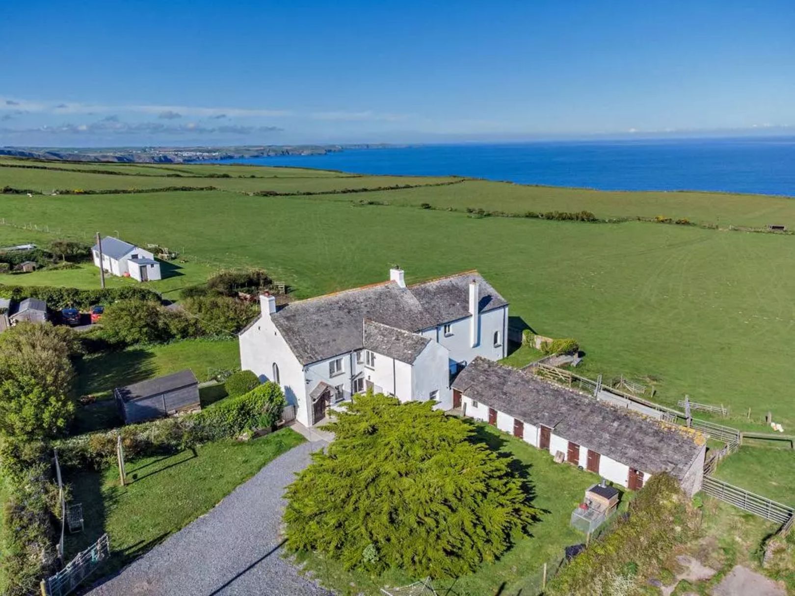 A white farmhouse with outbuildings, green fields and blue seas to the back