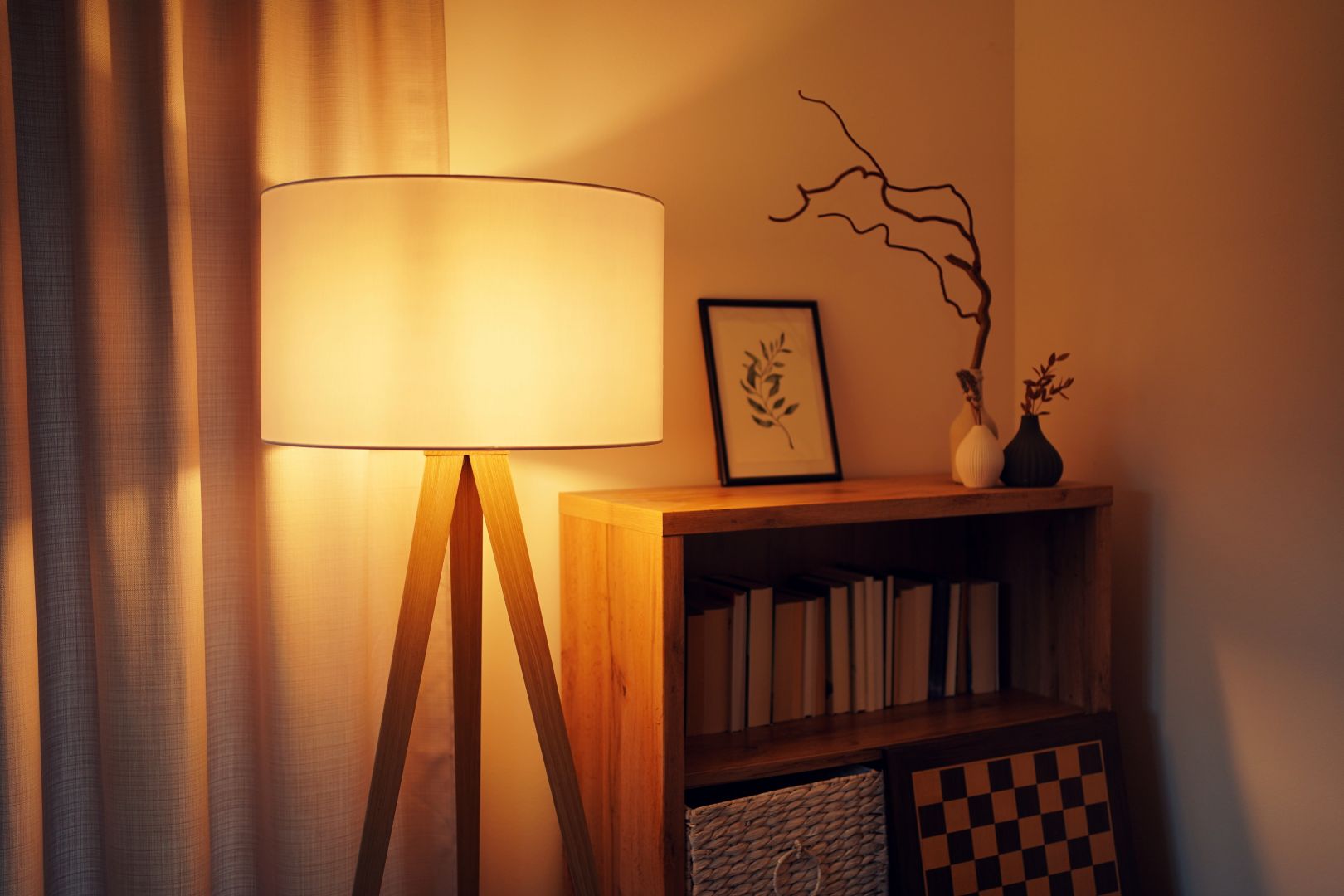 A warmly lit lamp in front of a wooden book shelf with a photo frame and decorations on top