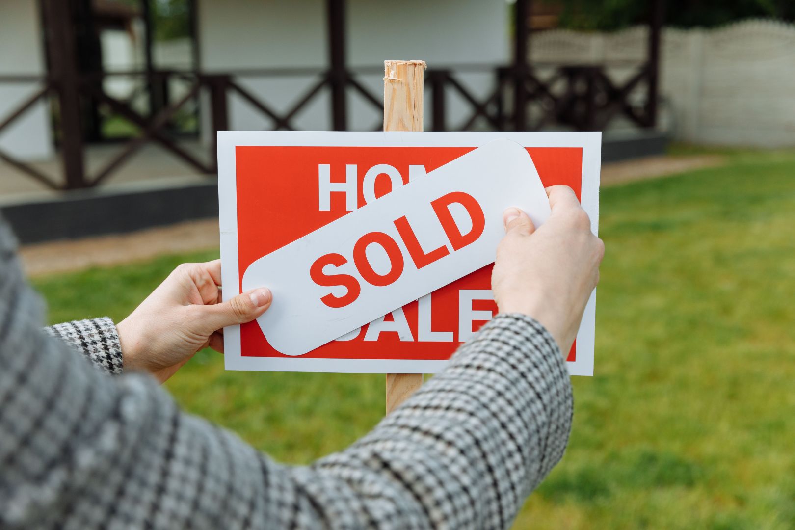 "House for sale sign" with a woman's hands placing a "sold" sign over the top