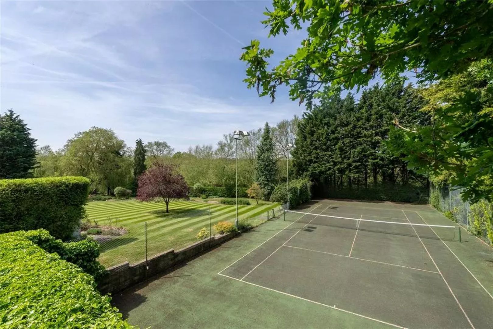 A hard tennis court next to green lawns