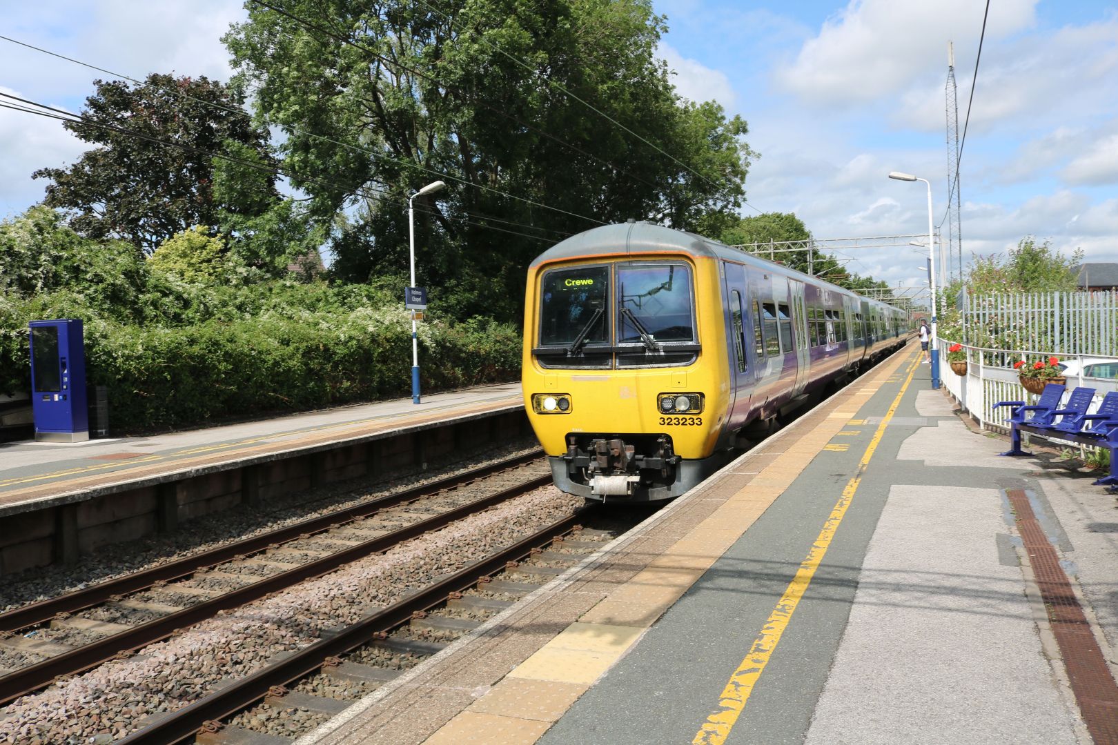 A train pulling into a station with trees and bushes in the background