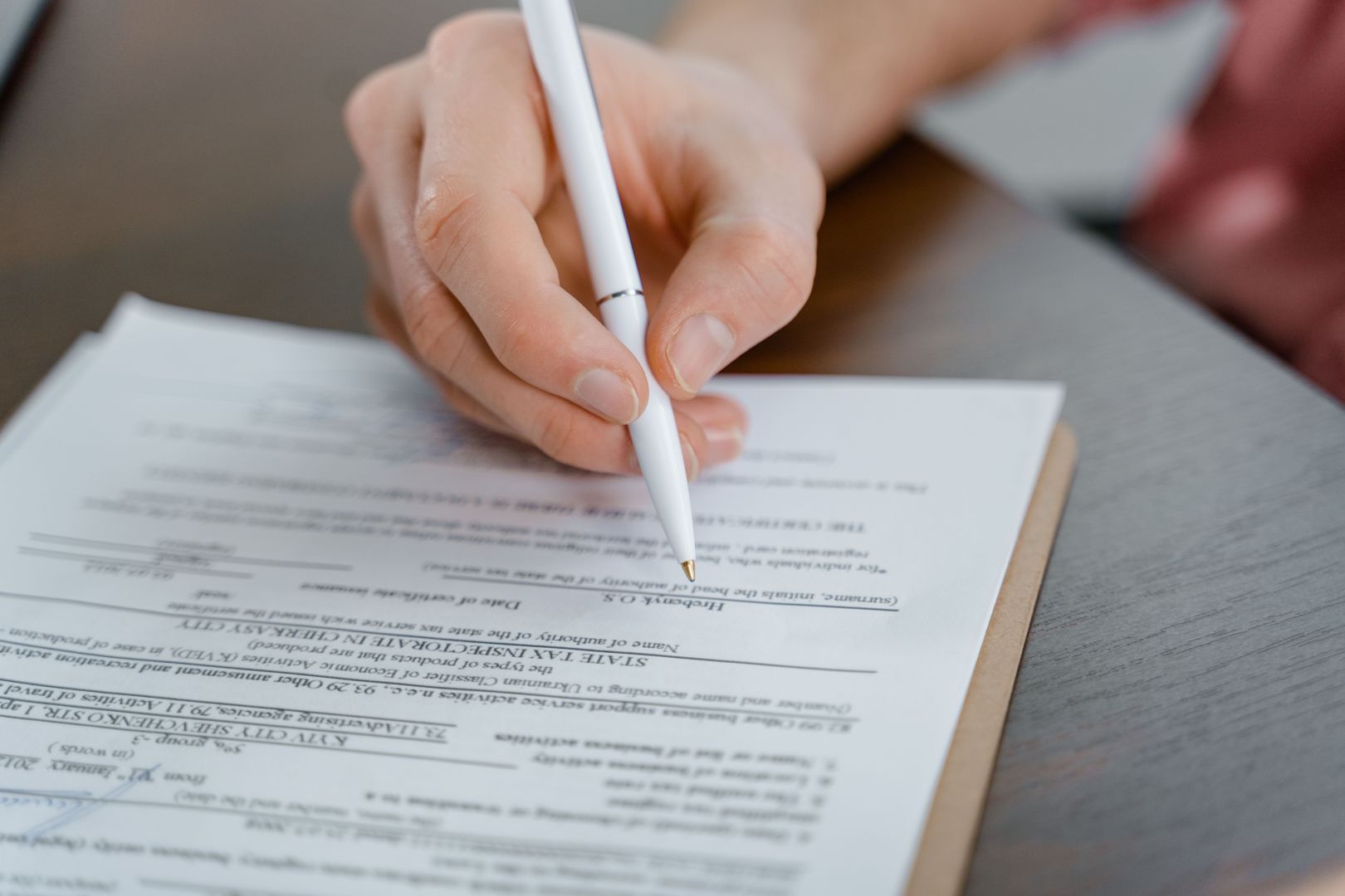 A hand signing a form with a pen