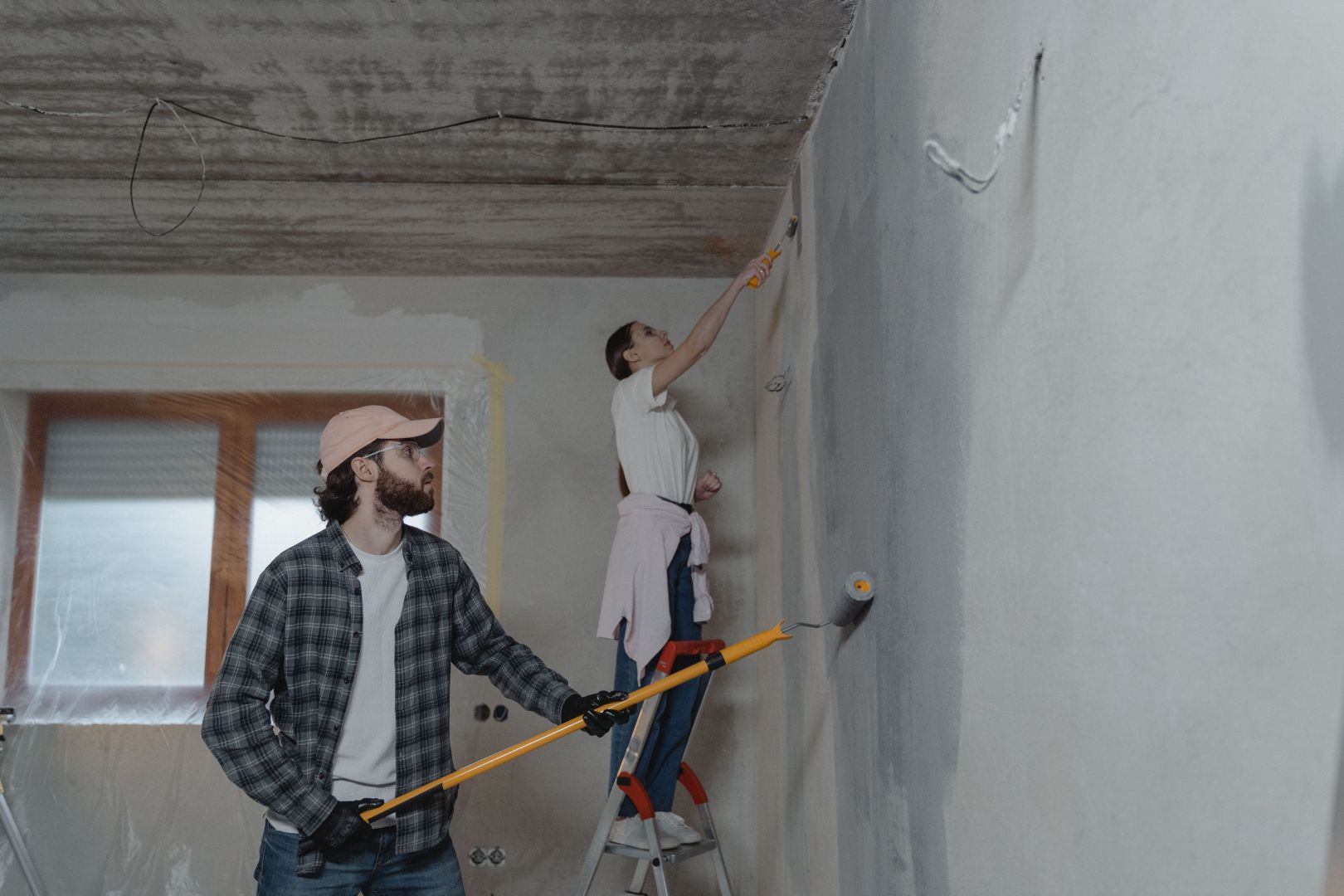 Two people, a man and a woman, painting a white wall with blue paint