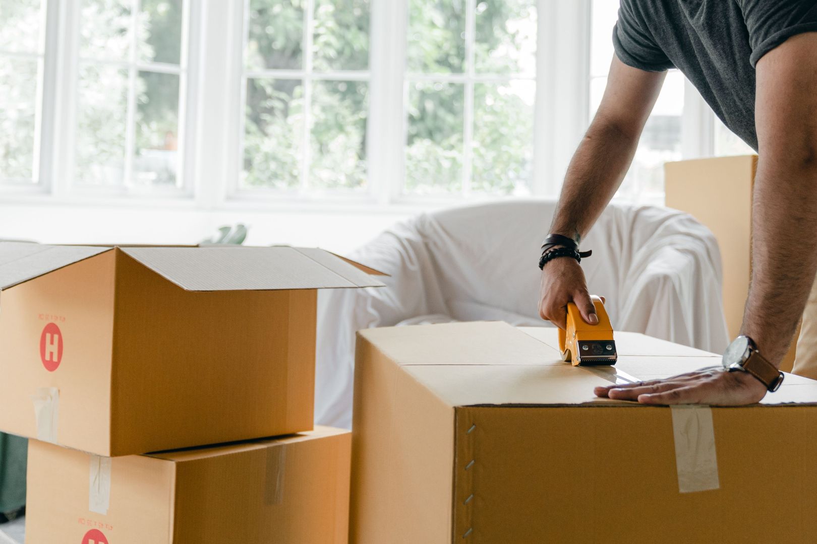 A man's arms are shown taping up a cardboard box to move house