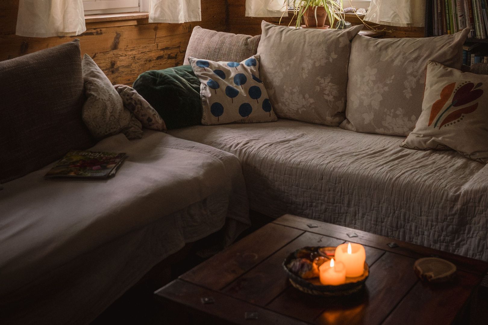 A corner sofa, draped with blankets and cushions, with two candles on a coffee table in front